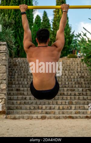 Primo piano ritratto da dietro il giovane latino senza camicia e pantaloni neri e maschera di allenamento al bar di un parco calistenico Foto Stock