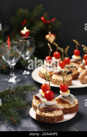 Crostini con aringhe salate, formaggi, uova di quaglia e pomodori ciliegini su crostini di segala su fondo scuro. Formato verticale. Primo piano Foto Stock
