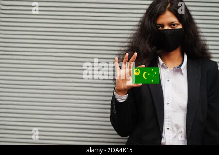 Donna asiatica all'usura formale e maschera nera proteggere faccia tenere Cocos (Keeling) Isole bandiera a portata di mano contro sfondo grigio. Coronavirus alla conce di paese Foto Stock