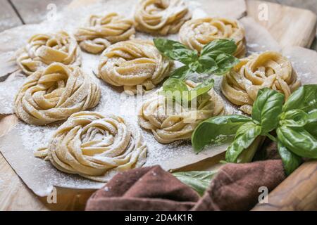 Pasta alluovo, Tagliatelle o fettuccine. Palline rotonde di pasta cruda sul tagliere di legno su sfondo nero Foto Stock