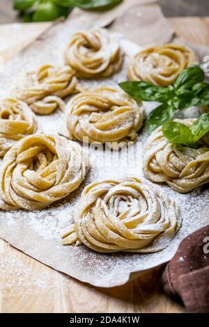 Pasta alluovo, Tagliatelle o fettuccine. Palline rotonde di pasta cruda sul tagliere di legno su sfondo nero Foto Stock