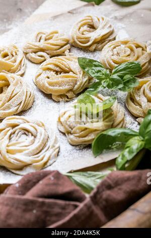 Pasta alluovo, Tagliatelle o fettuccine. Palline rotonde di pasta cruda sul tagliere di legno su sfondo nero Foto Stock