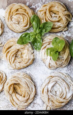 Pasta alluovo, Tagliatelle o fettuccine. Palline rotonde di pasta cruda sul tagliere di legno su sfondo nero Foto Stock