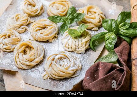 Pasta alluovo, Tagliatelle o fettuccine. Palline rotonde di pasta cruda sul tagliere di legno su sfondo nero Foto Stock