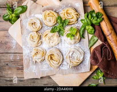 Pasta alluovo, Tagliatelle o fettuccine. Palline rotonde di pasta cruda sul tagliere di legno su sfondo nero Foto Stock