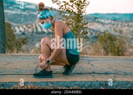 Ritratto di una giovane donna al parco legando i lacci delle sue sneakers che indossano una maschera Foto Stock