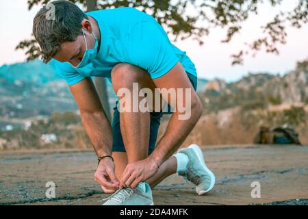 Ritratto di un giovane al parco legando i lacci delle sue sneakers che indossano un facemask Foto Stock