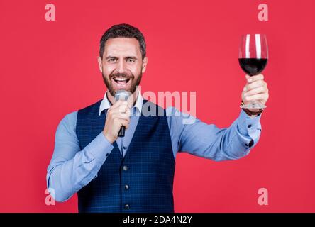 Chiedo che il banchetto continui. Toastmaster parla nel microfono sollevando un bicchiere di vino. Organizzare un banchetto. Cerimonia o celebrazione. Parlare in pubblico. Arte oratoria abilità nel linguaggio. Foto Stock