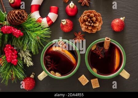 VIN brulé, bevanda alcolica invernale, due tazze d'epoca, ingredienti arancio e spezie e decorazioni natalizie su pietra nera, vista dall'alto. Foto Stock