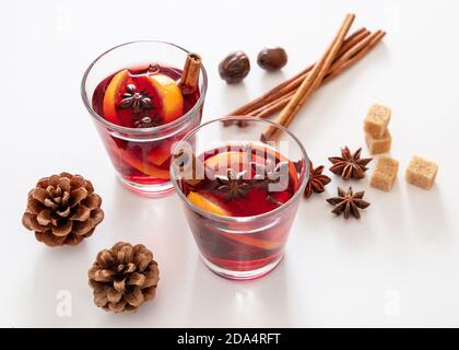 VIN brulé, bevanda alcolica invernale natalizia, due bicchieri, ingredienti arancio e spezie su sfondo bianco, vista closeup. Foto Stock