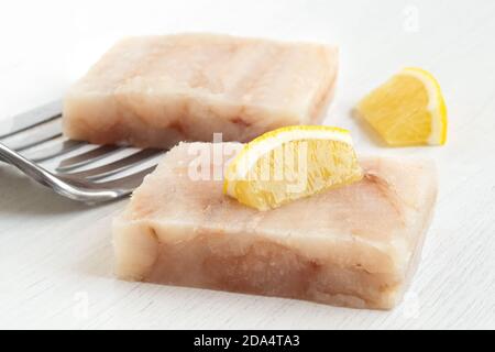 Due filetti di pesce surgelati con spicchi di limone e spatola in metallo su bianco. Foto Stock