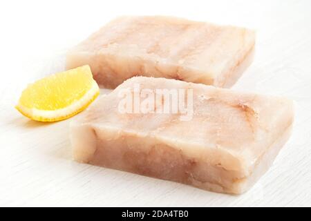 Due blocchi di filetto di pollock surgelati con un cuneo di limone isolato su bianco. Foto Stock