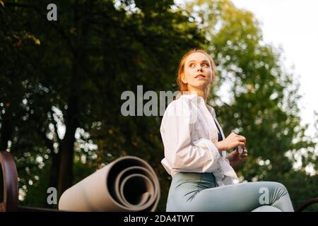 Giovane donna dai capelli rossi rilassata seduta sulla panchina nel parco cittadino. Happy femminile ha vacanze all'aperto. Foto Stock