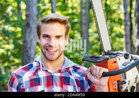 Forte lumberjack con motosega in una camicia in plaid. Lumberjack lavoratore a piedi nella foresta con motosega. Taglialegno con motosega su segheria Foto Stock