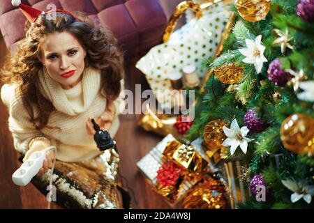 Buon Natale. Vista superiore della donna trendy di 40 anni in gonna di paillettes d'oro e maglione con presa elettrica tee vicino albero di Natale e scatole regalo. Foto Stock