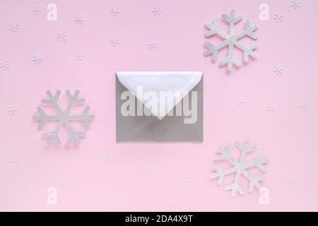 Busta argento con biglietto d'auguri e fiocchi di neve su sfondo rosa pastello. Lettera con congratulazioni, lettera a Babbo Natale. Natale o Capodanno Foto Stock