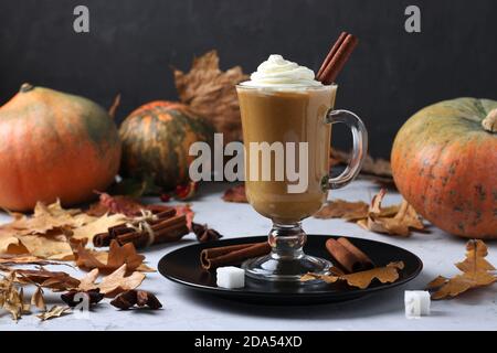 Una tazza di latte di zucca di vetro con spezie e schiuma cremosa su sfondo scuro con zucche e foglie d'autunno. Primo piano. Foto Stock