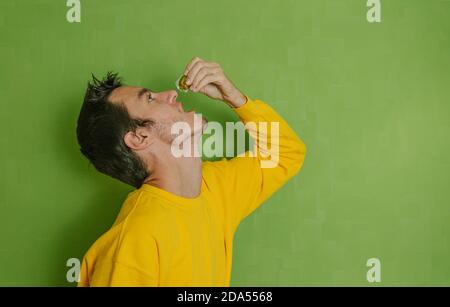 Giovane uomo che beve olio d'oliva in una piccola fiala di plastica su sfondo verde, concetto di stile di vita sano Foto Stock