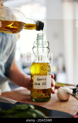 Donna che versa olio d'oliva in una bottiglia contenente aglio Foto Stock