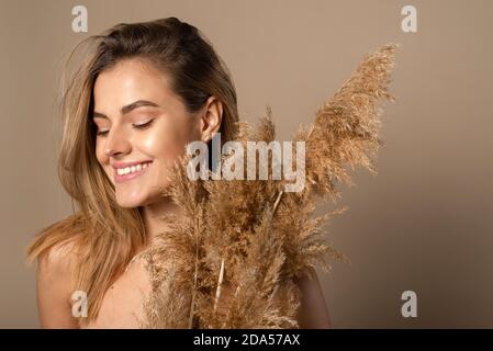 Felice bella modella sorridente giovane che tiene in mano l'erba secca di pampas. Il concetto di cosmetici naturali da grani di grano. Cura della pelle. Foto Stock