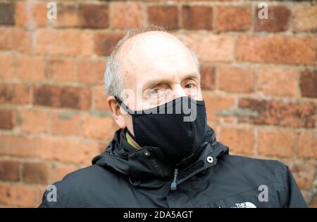 Primo piano di un uomo anziano o anziano che indossa una maschera nera o una copertura facciale e anorak nero all'esterno. Foto Stock