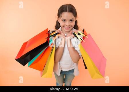 Esperto di moda. Bambino graziosi negozi expert aiuta a portare pacchetti durante lo shopping. Little Shop esperto. Shopping ragazza ama fare shopping. Kid ragazza faccia felice porta mazzetto pacchetti sfondo giallo. Foto Stock