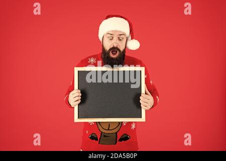 Incredibile. Annuncio d'inverno. Lavagna per informazioni. Man tenere lavagna vuota copia spazio. Guy babbo natale sfondo rosso. Evento invernale. Vacanze invernali. Santa Claus hat con la pubblicità. Foto Stock