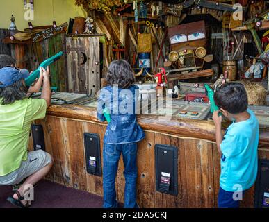 Vista posteriore dei bambini che utilizzano fucili giocattolo con bersagli digitali esposti su oggetti in collina presso la galleria di Gatlinburg, TN, nelle montagne fumose Foto Stock