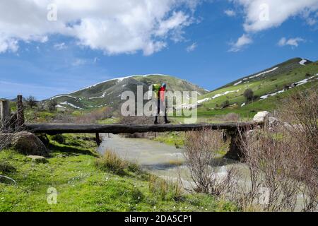 Escursionista con zaino che attraversa il primitivo ponte di tronchi di legno sul torrente nel Parco Nebrodi, Sicilia Foto Stock