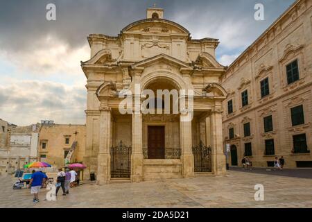I turisti con ombrelli colorati cercano di sfuggire alla pioggia di fronte alla Chiesa di Santa Caterina a la Valletta, sull'isola mediterranea di Malta. Foto Stock