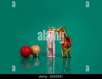 palline di nuovo anno, pacchetto di banconote in dollari con monete e piccole scatole regalo su sfondo verde. Foto Stock
