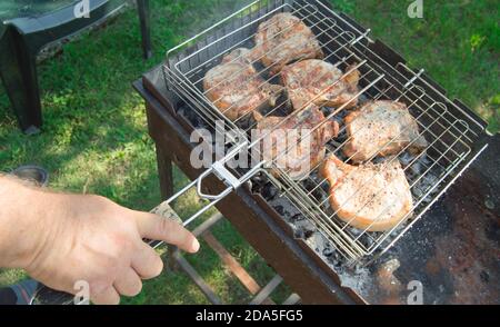 Primo piano di una mano dell'uomo che prepara carne fritta, all'aperto, in estate, sullo sfondo dell'erba Foto Stock