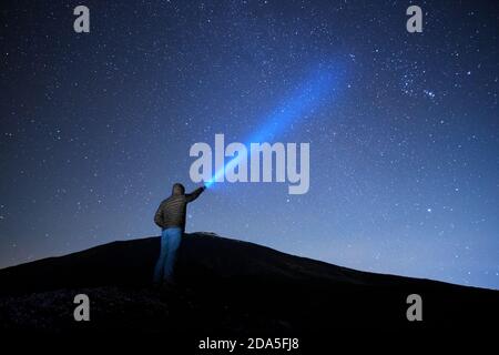 Uomo che punta la torcia blu al cielo stellato nel Parco dell'Etna, Sicilia Foto Stock