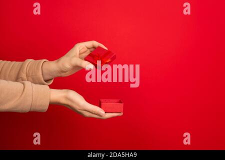 Mano femmina tenere aperta rosso piccola scatola di gioielli su sfondo rosso. Concetto di regalo, regalo o e-shopping. Banner con spazio per la copia Foto Stock