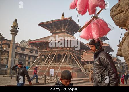 Patan, Nepal, gennaio 2016. I bambini vendono caramelle di fronte ai templi punteggiati in Piazza Durbar dopo il terremoto del 2015 aprile. Foto Stock