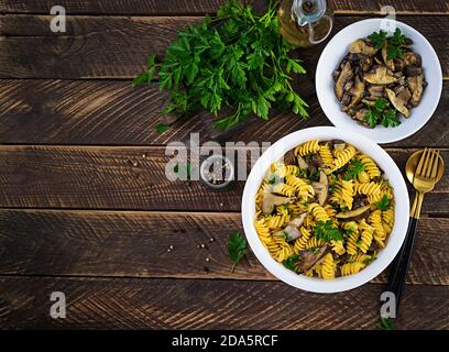 La pasta dei fusilli è priva di glutine con funghi di bosco su un piatto bianco. Cibo vegetariano / vegano. Cucina italiana. Vista dall'alto, disposizione piatta, spazio per la copia Foto Stock