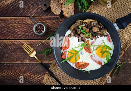 Colazione gustosa: Uova fritte, funghi della foresta, pomodori e rucola. Pranzo cibo. Vista dall'alto, overhead, spazio per la copia Foto Stock