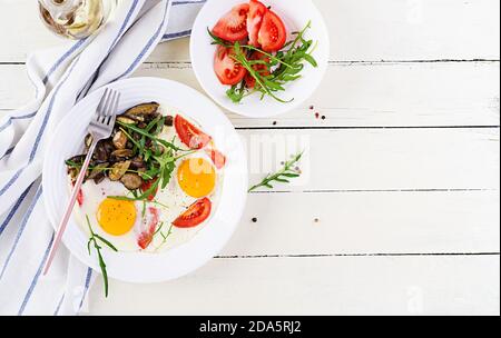 Colazione gustosa: Uova fritte, funghi della foresta, pomodori e rucola. Pranzo cibo. Vista dall'alto, overhead, spazio per la copia Foto Stock