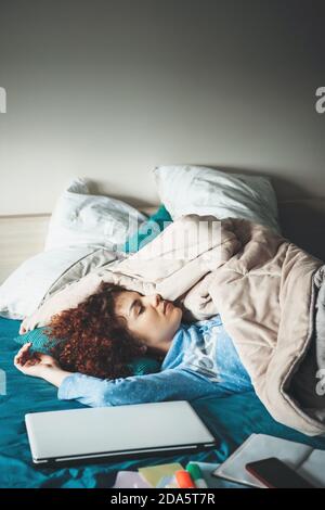 Donna caucasica stanca con capelli ricci che si rilassano dopo aver fatto i compiti sul computer portatile nel letto Foto Stock