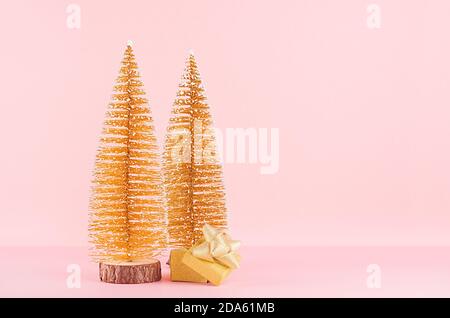 Alberi di natale con glitter oro con scatola regalo scintillante con prua su elegante sfondo rosa pastello. Foto Stock