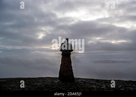 Un uomo si trova su un punto di trig in cima a MAM Tor, vicino a Castleton nel Peak District National Park nel Derbyshire. Foto Stock