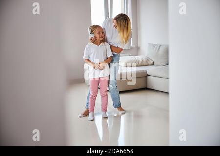 Buona donna in vestiti casual che parla con la bambina a casa Foto Stock