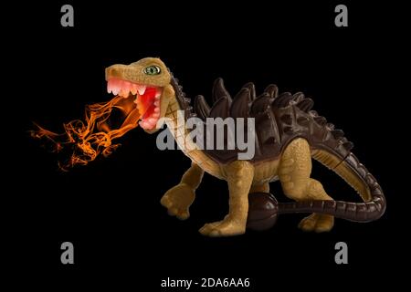 Dinosauro giocattolo che respira il fuoco. Giocattolo per bambini, personaggio animale di plastica isolato su sfondo nero, composito fantasy. Dinosauro con Spikes e coda club Foto Stock