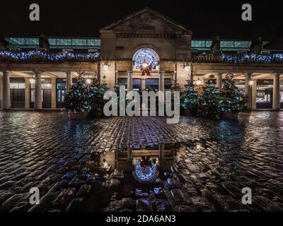 La pioggia e i riflessi durante la notte cadono intorno all'albero di natale a Covent Garden durante il secondo blocco a Londra. Foto Stock