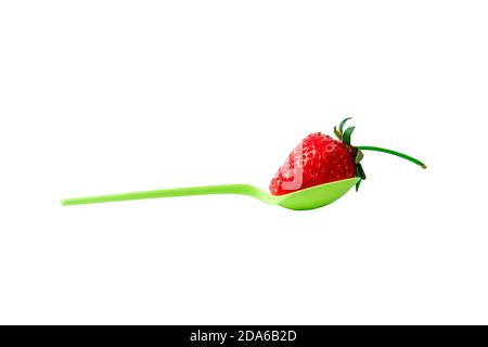 Una sola fragola matura rossa che si stacca su un cucchiaio di plastica verde brillante e si leva su uno sfondo bianco isolato. Posiziona per testo o banner Foto Stock