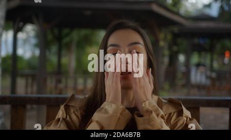 Bella donna sedendosi nel gazebo, sembra che abbia un freddo durante la stagione influenzale, guardando la macchina fotografica e starnutendo e sorridendo, raffreddore influenza e co Foto Stock