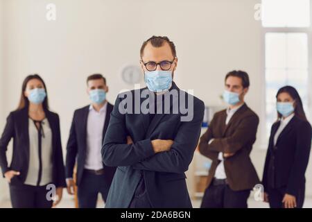 Ritratto dei lavoratori in ufficio guidati da un giovane leader aziendale che indossa maschere di protezione sul lavoro. Foto Stock