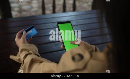 Giovane donna seduta nel gazebo shopping online con carta di credito e telefono su Internet, video di primo piano schermo verde, stile di vita tecnologia e. Foto Stock