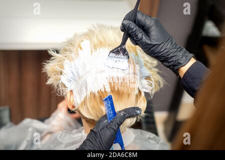 Vista posteriore delle mani di capelli stylist tintura di giovane donna di colore bianco in parrucchiere Foto Stock