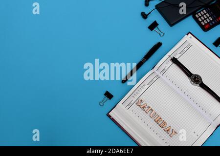 Scrivania da tavolo con vista dall'alto. Flat Lay Workspace con orologio, calcolatrice, penna, graffetta, notebook, matita, forniture per ufficio su sfondo blu Foto Stock